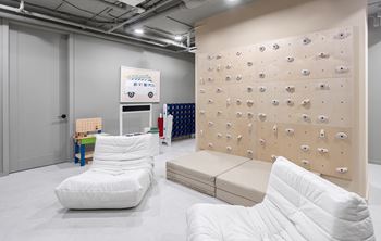 A white chair sits in front of a climbing wall in a room with white walls and floors.